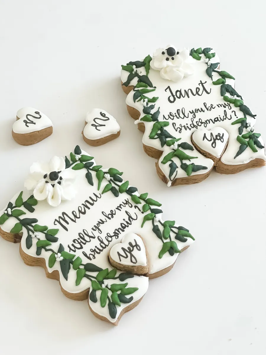 Will you be my bridesmaid proposal cookies with green vine borders, white flowers and yes and no heart cookies