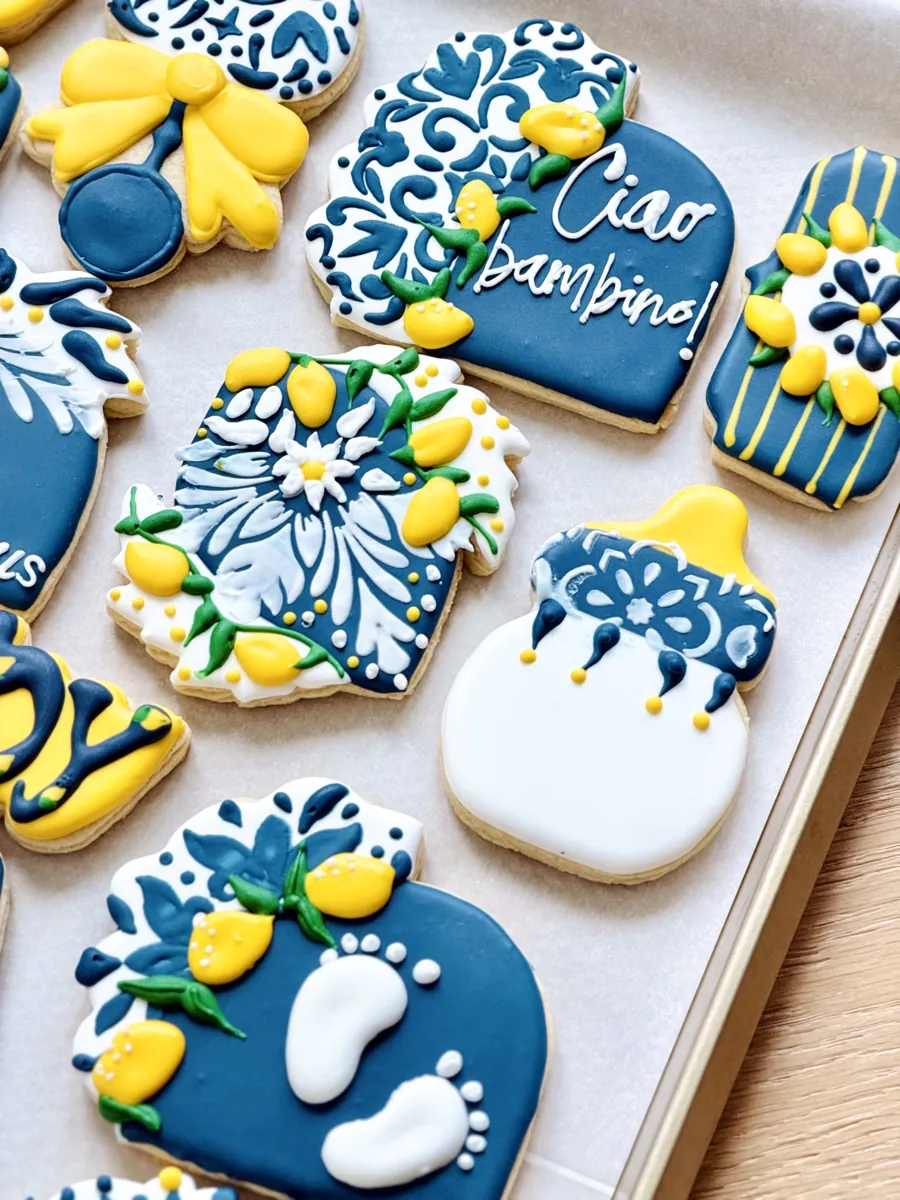 Italian lemon themed baby shower cookies in navy and yellow with Ciao bambino lettering, baby bottle and baby feet
