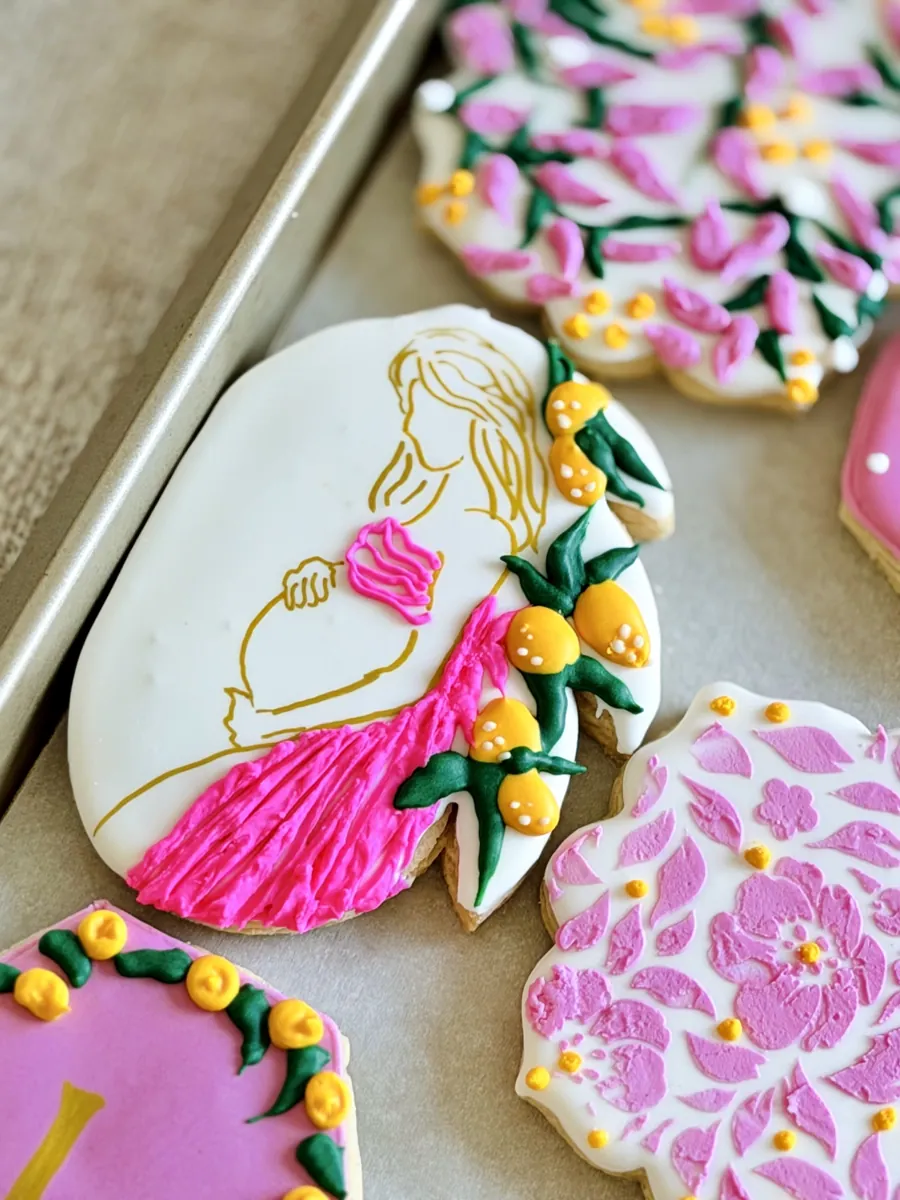 Baby shower cookie with a gold line drawing of an expecting mother, pink flowers and lemons
